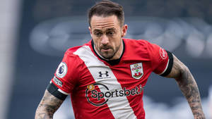 身穿紅白球衣的足球運動員在比賽中奔跑，手臂上有紋身。 — 足球 壁紙