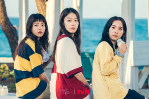 三位年輕女性穿著色彩繽紛的衣服，在日落時分坐在海邊。