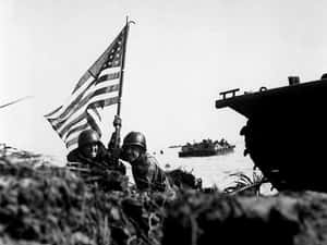 兩名士兵在軍事登陸期間在海灘上舉起美國國旗。