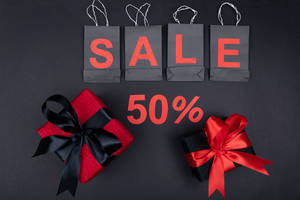 黑色購物袋拼出SALE，附有50%折扣文字，以及兩個附有紅色和黑色蝴蝶結的包裝禮物。