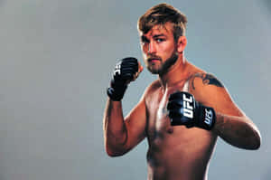 一名赤裸上身的男性MMA拳手戴著黑色UFC手套，在工作室中舉起拳頭擺姿勢。
