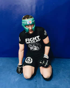 一名男性戰士跪在藍色軟墊上，戴著綠色頭盔和黑色裝備。