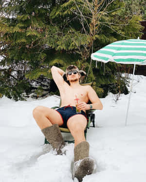 穿著泳褲和毛帽的男子在雪地上放鬆，有飲料和傘。