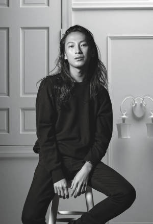 一個長髮的人坐在凳子上，黑白攝影棚肖像。