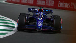 藍色和紅色的 Formula 1 賽車在夜間賽道上疾馳，賽道設有綠色路緣。 — 賽車 壁紙