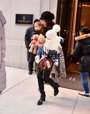 女士抱著兩個拿著泰迪熊的幼兒離開四季酒店。