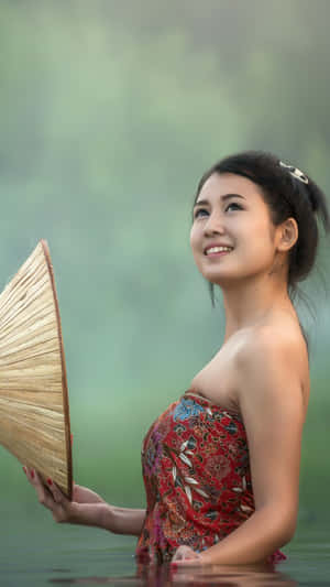 一位身穿紅色連衣裙的女子在迷霧的水中手持竹扇。