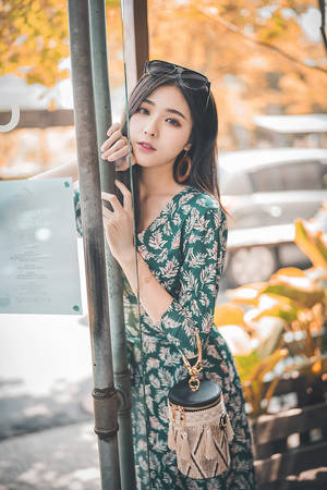 身穿花卉連衣裙的年輕女性靠著柱子，身後有秋葉。