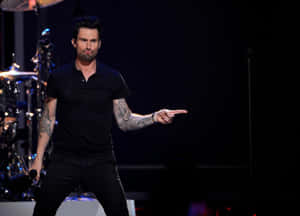 Adam Levine 在舞台上表演，指著並露出紋身。 — 省電 壁紙