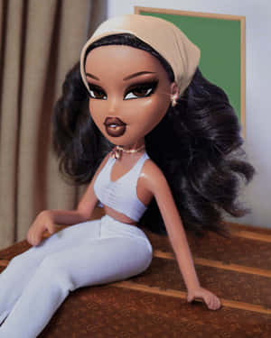 穿著白色家居服的 Bratz 公仔坐在圖案表面上，背景有窗簾和綠色牆壁。