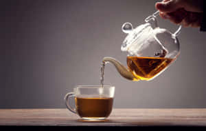手將琥珀色茶從玻璃茶壺倒入透明杯中，木桌。