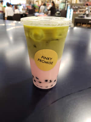 一杯分層的粉紅和綠色泡泡茶飲料，內有波霸珍珠，放在深色桌子上的塑膠杯中。 — iPad Air 壁紙