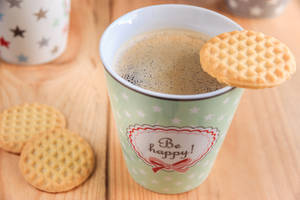 一個寫著「Be happy!」的綠色杯子，裝著咖啡，邊緣放著一塊窩夫曲奇。