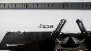 復古打字機喺白色紙上打出「June」一詞，上面有金屬尺。 — 夏日氣息 壁紙