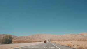 紅色汽車在沙漠公路上，背景有山脈和藍天，黃昏時分