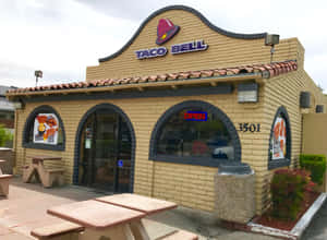 Taco Bell餐廳外觀，設有野餐桌和營業標誌。