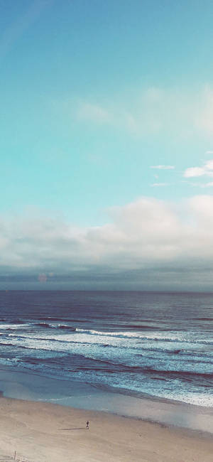 一個孤獨的人在海灘上行走，有海浪和多雲的天空。