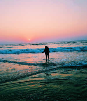 日落時分站在海浪中的人，天空呈粉紅色和橙色 — 夏日氣息 壁紙