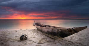 夕陽下沙灘上的木製獨木舟，伴隨著火紅的天空和寧靜的水面。