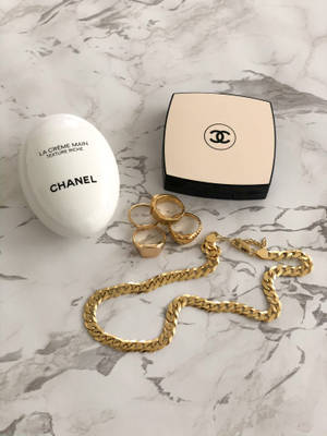 Chanel護手霜粉餅和黃金首飾在大理石背景上