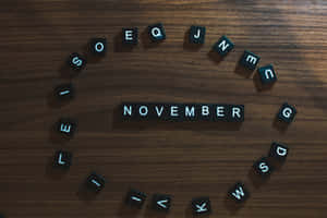 黑色字母瓷磚拼出November，排列在木質表面上，周圍散落著字母瓷磚。
