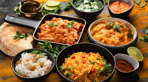 木桌上擺放著咖喱、米飯、印度薄餅和香料的彩色印度餐。