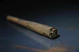 一個已點燃的大麻煙捲在深色反光表面上，煙霧裊裊升起。