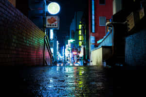 霓虹燈光在濕漉漉的人行道上反射，狹窄的日本城市小巷夜景。 — 東京 壁紙