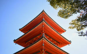 藍天白雲下，綠樹枝葉間，一座橙色寶塔，屋頂層層疊疊。