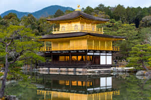 金色寺廟倒映在池塘中，背景有綠樹和山脈 — 日本 壁紙
