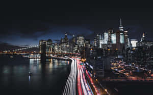 夜間城市景觀，帶有車流的光跡和海濱沿岸發光的摩天大樓。