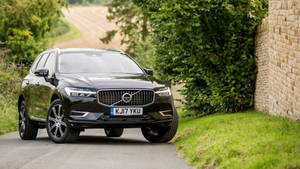 黑色沃爾沃XC60 SUV在鄉村道路上，旁邊有石牆和樹木。
