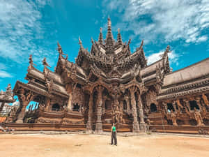 一個人站在藍天下巨大而精雕細琢的木製寺廟前。 — 建築 壁紙