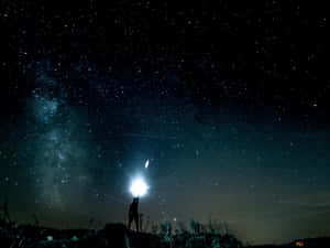 一個人在有銀河和流星的星空下拿著手電筒的剪影。 — 星星 壁紙