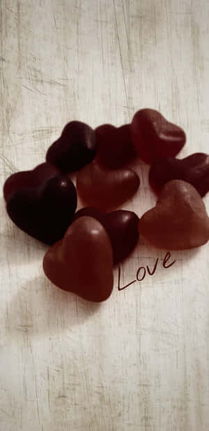 有刮痕的木頭上放著光澤的紅色心形糖果，旁邊寫著 'Love'。 — 鼓舞人心的 壁紙