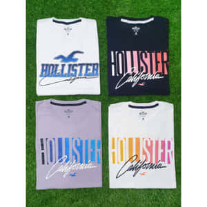 綠色草地上四件摺疊好的Hollister California T恤。