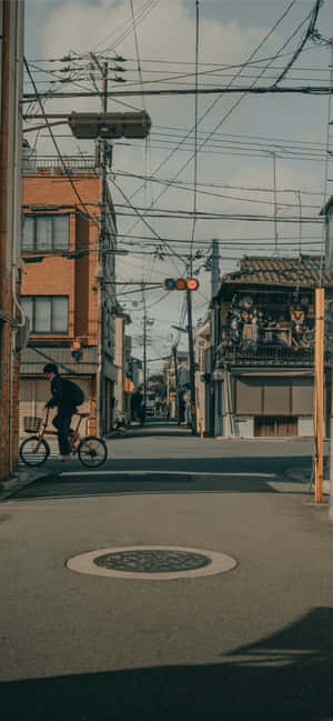 一個人在有建築物和電線的狹窄城市街道上騎單車。