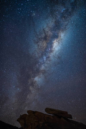 在繁星點點的夜空下，銀河系在黑色岩石剪影上方閃耀