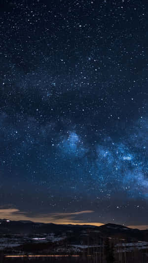 星空之夜，銀河橫跨積雪的山脈和遠處的燈光。 — 夜空 壁紙
