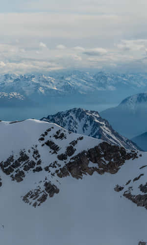 白雪覆蓋的山峰在陰雲密布的天空下，遠山山脊在煙霧繚繞的大氣中。