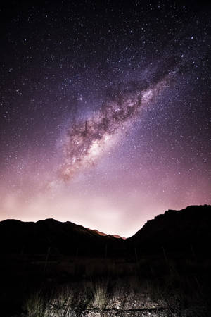銀河系在星空下照耀著山脈剪影。 — 紫色 iPhone 壁紙
