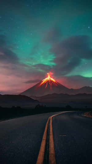 一條道路彎向一座在發光極光天空下熾熱噴發的火山。 — 風景動圖 壁紙