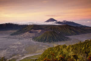 日出時分的火山山脈，有雲朵和綠色植被。 — MacBook Air M4 壁紙