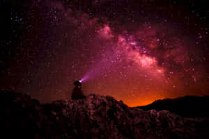人坐在岩石上，用頭燈照亮色彩繽紛的星空 — 可愛星系 壁紙