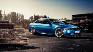 藍色BMW M3跑車停泊在堆疊木頭旁邊，夕陽西下。