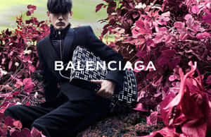 身穿黑色西裝的男子手持 Balenciaga 手袋，被洋紅色樹葉包圍。