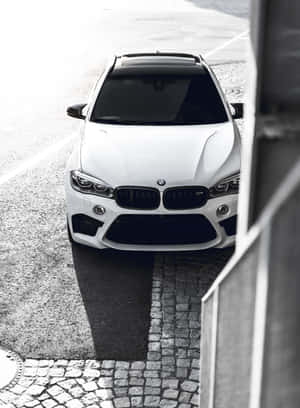 白色BMW SUV停放在鵝卵石街道上，以現代建築為框架。 — 2048x2732 壁紙
