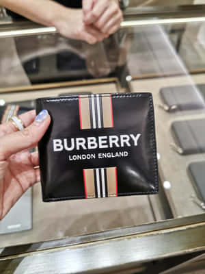 手在商店展示中拿著一個帶有標誌和條紋的黑色 Burberry 銀包。 — 美學波希米亞動態圖 壁紙