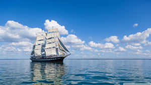 高桅帆船在平靜的海洋上航行，天空湛藍，白雲朵朵