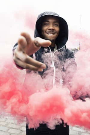 穿連帽衫的男人微笑著在城市的行人道上伸手穿過粉紅色煙霧
